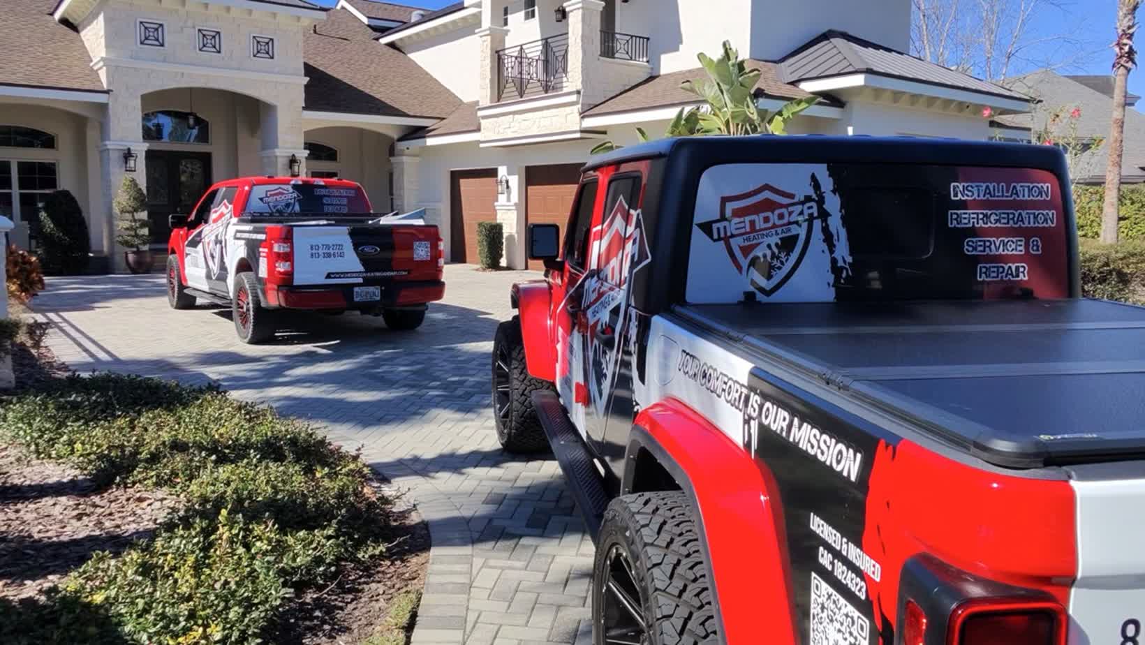 Two wrapped Mendoza Heating and Air trucks parked in front of a Tampa home